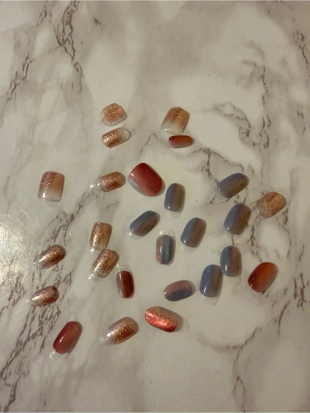 Assorted Press-On Nail Set in Rose Gold, Coral, and Blue with black pouch.